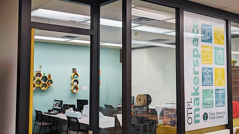 The orion library makerspace. The room shows different computer stations on tables in the room with equipment like a Cricut on the table as well. There are decorative creative projects on the wall.