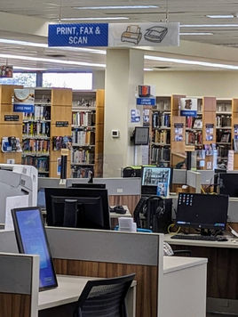 The adult services area of the Orion Library with a scanner, printer, many computers, and behind the computers, five rows of bookstacks.