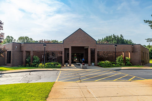 Exterior of the front of the Orion Library Building on a sunny day with a blue and cloudy sky and vibrant green grass